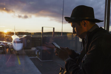 Junger Mann benutzt Handy auf dem Flughafen bei Sonnenuntergang - KKAF01804