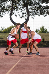 Drei junge Männer spielen Basketball auf einem Platz im Freien - STSF01739