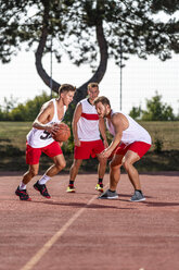 Three young men playing basketball on an outdoor court - STSF01739