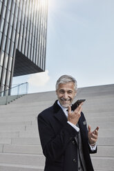 Porträt eines zufriedenen Geschäftsmannes, der vor einer Treppe steht und telefoniert - RORF01472