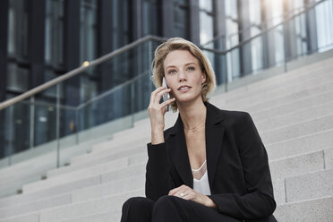 Porträt einer jungen Geschäftsfrau, die auf einer Treppe im Freien sitzt und telefoniert - RORF01484