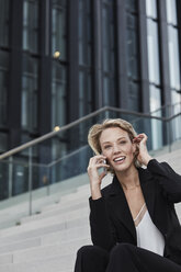 Porträt einer lächelnden jungen Geschäftsfrau, die auf einer Treppe im Freien sitzt und telefoniert - RORF01485