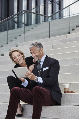 Portrait of two businesspeople sitting together on stairs looking at tablet having fun stock photo