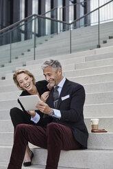 Portrait of two businesspeople sitting together on stairs looking at tablet having fun - RORF01502