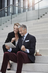 Zwei Geschäftsleute sitzen zusammen auf einer Treppe und schauen auf ein Tablet - RORF01504
