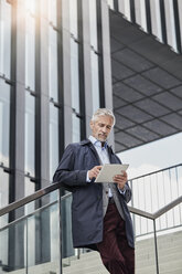 Porträt eines reifen Geschäftsmannes, der auf einer Treppe vor einem modernen Bürogebäude steht und ein Tablet benutzt - RORF01506