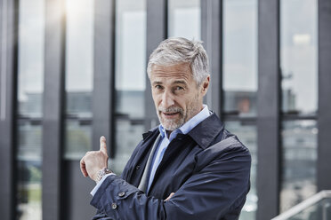 Germany, Duesseldorf, portrait of businessman pointing at office building at Media Harbour - RORF01514