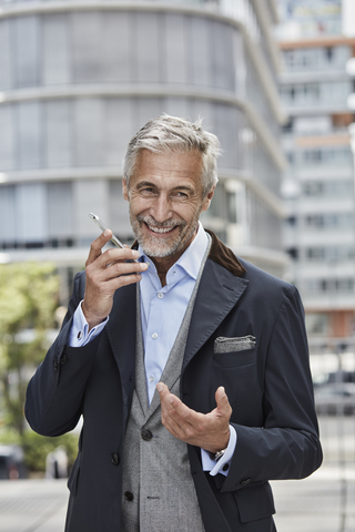 Deutschland, Düsseldorf, Porträt eines lachenden reifen Geschäftsmannes, der mit einem Mobiltelefon spricht, lizenzfreies Stockfoto