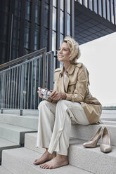 Portrait of young fashionable woman with digital camera sitting barefoot on stairs - RORF01543