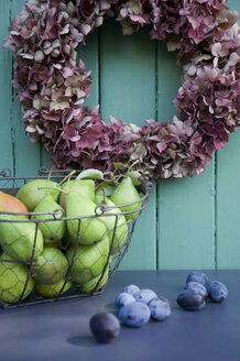 Wreath with hortensias, pears in wire basekt and plums on wood - GISF00385