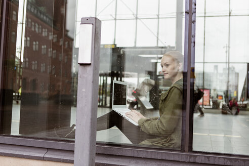 Nachdenkliche Frau, die einen Laptop benutzt und durch ein Fenster am Bahnhof schaut - MASF08614