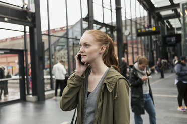 Junge Frau, die mit einem Freund im Hintergrund in der Stadt mit einem Mobiltelefon spricht - MASF08616