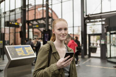 Porträt einer jungen Frau, die ein Handy in der Hand hält, während sie am Bahnhof steht - MASF08617