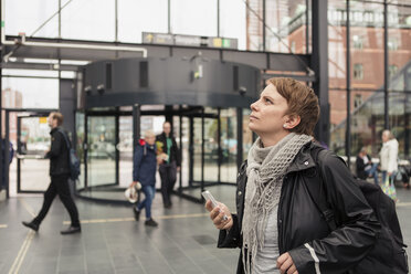 Nachdenkliche Frau hält ihr Smartphone in der Hand, während sie an einem Gebäude in der Stadt nach oben schaut - MASF08618