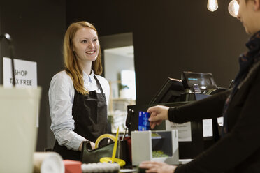 Lächelnde Besitzerin schaut den Kunden an, während sie an der Kasse des Ladens steht - MASF08631