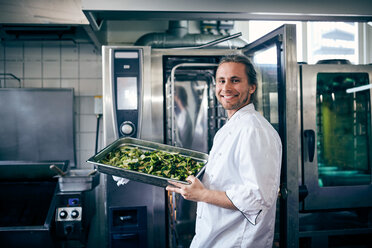 Porträt eines selbstbewussten Kochs mit Brokkoli im Backblech in einer Großküche - MASF08666