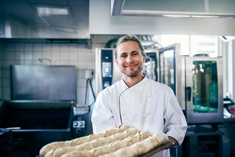 Porträt eines selbstbewussten Kochs, der in einer Großküche Brote backt, lizenzfreies Stockfoto