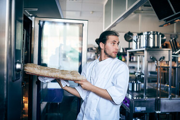 Männlicher Koch, der Brot in den Ofen schiebt, während er in die Großküche schaut - MASF08670
