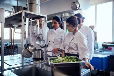 Das Team des Küchenchefs beobachtet einen Kollegen bei der Zubereitung von Speisen in einer Großküche - MASF08676