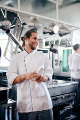 Lächelnder männlicher Koch, der eine Serviette in einer Großküche hält - MASF08681
