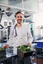 Portrait of smiling male chef holding containers of vegetables in kitchen - MASF08690