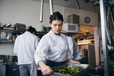 Mittlere erwachsene weibliche Köchin hält Backblech mit Brokkoli in einer Großküche - MASF08696