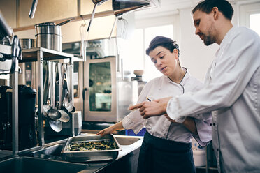 Male and female chefs reading order ticket while preparing food in commercial kitchen - MASF08699