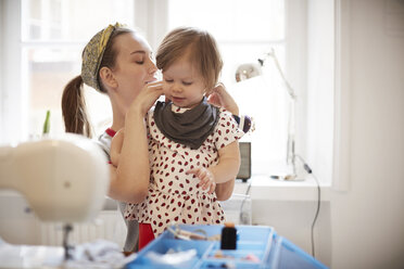 Female tailor tying scarf on daughter's neck while sitting at home - MASF08721