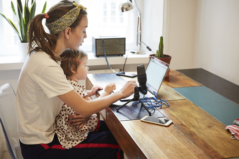 Podcaster sitzt mit Tochter bei der Vermarktung über den Laptop zu Hause, lizenzfreies Stockfoto