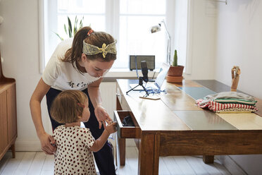 Podcaster looking at daughter opening drawer while standing by table - MASF08735