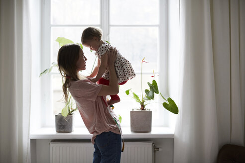 Seitenansicht einer Modedesignerin, die ihre Tochter bei sich trägt, während sie zu Hause am Fenster steht - MASF08745