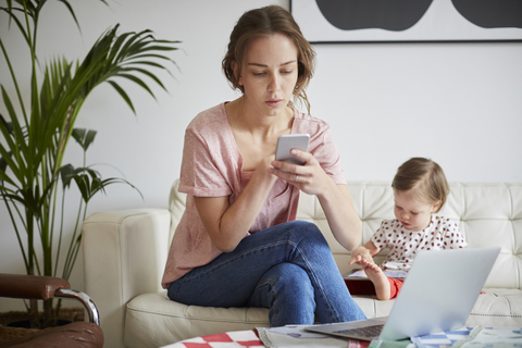 Fashion designer using mobile phone while sitting with daughter on sofa at home stock photo