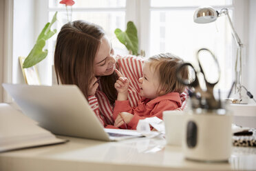 Lächelnde Frau im Gespräch mit ihrer Tochter, während sie zu Hause am Laptop arbeitet - MASF08762