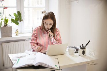 Female accountant using laptop while doing paperwork at home - MASF08768