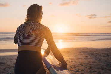 Rückansicht einer Frau mit Surfbrett, die bei Sonnenuntergang am Strand in Richtung Meer läuft - MASF08776