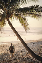 Rückansicht eines Mannes mit Surfbrett, der am Strand auf das Meer zugeht - MASF08778