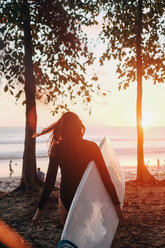 Rückansicht einer reifen Frau mit Surfbrett, die bei Sonnenuntergang am Strand spazieren geht - MASF08779