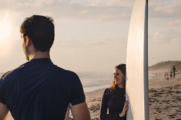 Young man with female friend holding surfboard at beach during sunset - MASF08789