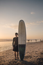 Junger Mann mit Surfbrett am Strand bei Sonnenuntergang in voller Länge - MASF08792