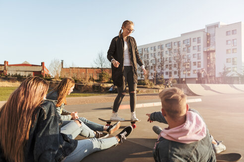 Freunde betrachten ein Teenager-Mädchen beim Skateboardfahren in einem Park in der Stadt - MASF08812