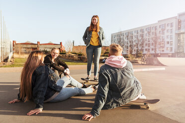 Freunde sitzen in einem Skateboard-Park und sprechen mit einem Mädchen, das an einem Gebäude steht - MASF08814