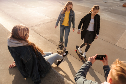 Hoher Blickwinkel eines Teenagers, der seine Freunde beim Skateboarden im Park fotografiert, lizenzfreies Stockfoto
