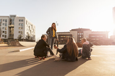 Freunde schauen auf einen Teenager, der einem Mädchen auf einem Skateboard in der Stadt sein Handy zeigt - MASF08818