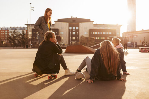 Teenager-Mädchen sitzt auf dem Skateboard und unterhält sich mit Freunden im Park an einem sonnigen Tag - MASF08819