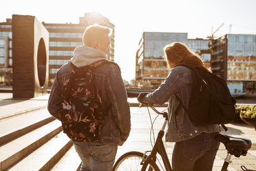 Teenage boy walking with friend holding bicycle in city during sunny day - MASF08822