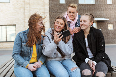 Smiling teenage girl taking selfie with friends through mobile phone against building - MASF08825