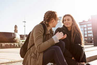 Teenage girls talking while sitting on steps in city during sunny day - MASF08828