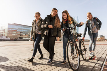 Teenage talking to friend holding bicycle while boy skateboarding at city - MASF08829