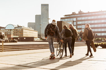 Rückansicht von Freunden mit Fahrrad und Skateboard in der Fußgängerzone in der Stadt gegen den Himmel - MASF08831
