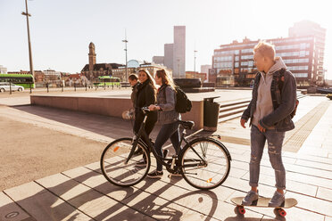 Teenage boy skateboarding while walking with girl holding bicycle on pedestrian zone at city - MASF08835